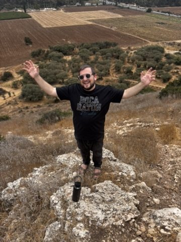 Jacob with his arms spread wide on a rock above the patchwork fields